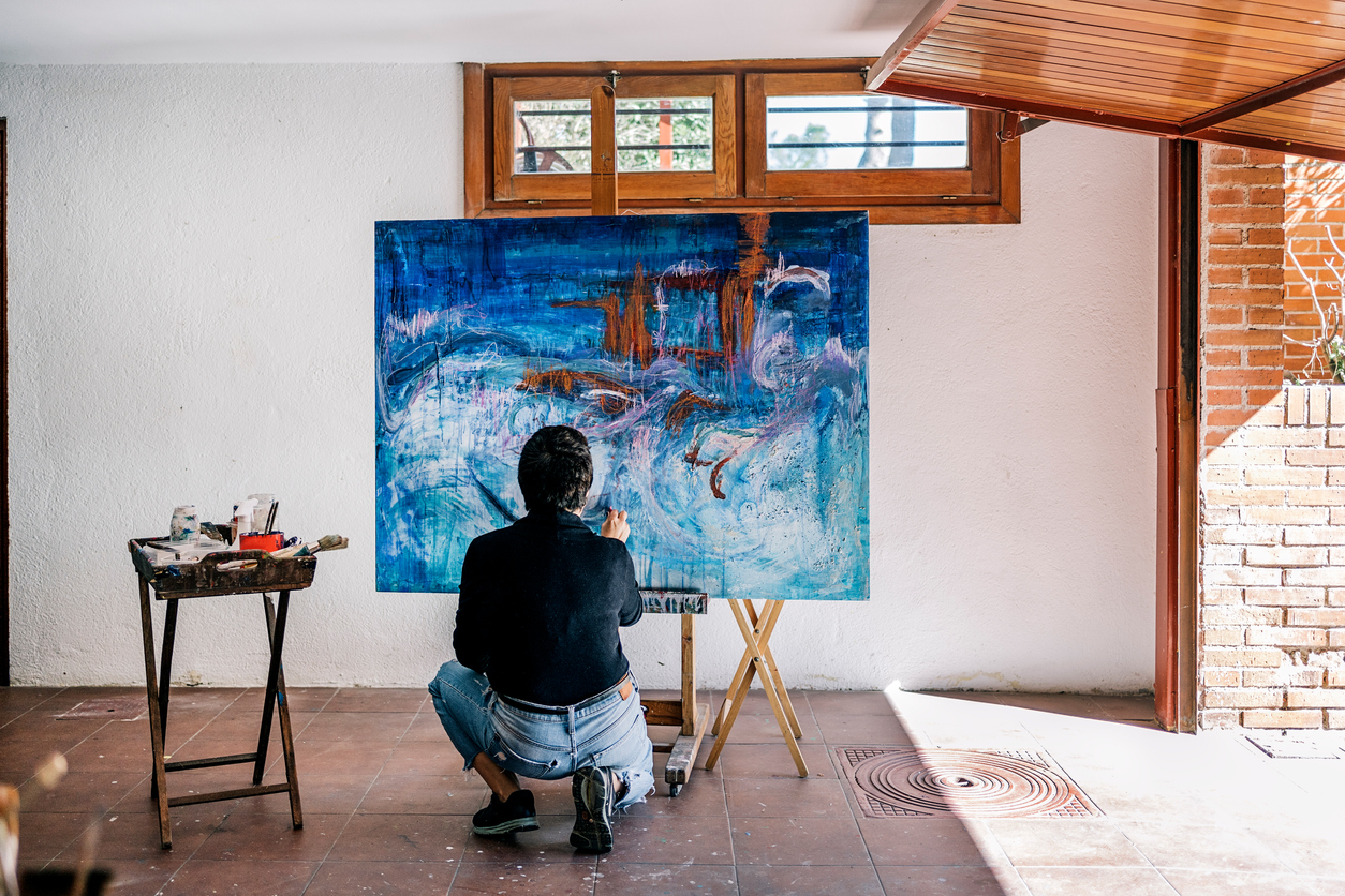 Unrecognized female painter relaxing in her garage painting with blue paint in a big canvas.