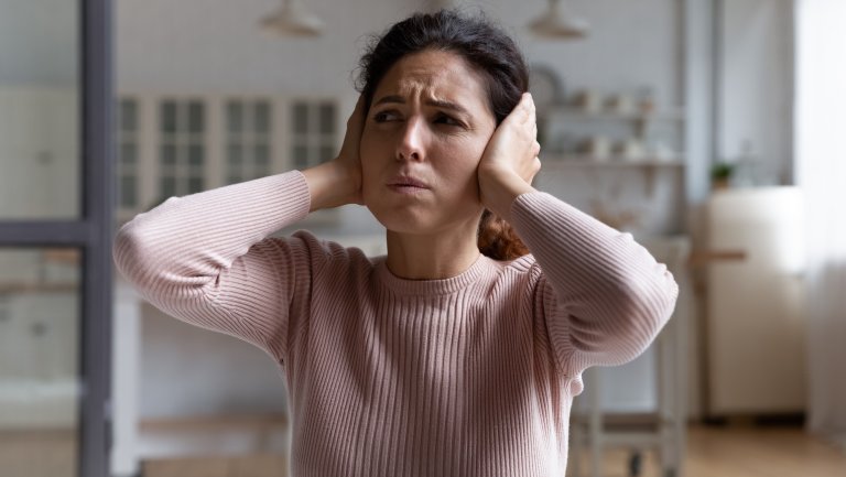 Unhappy millennial Caucasian female renter or tenant cover ears with hands hate noise at home or apartment. Upset angry woman feel depressed frustrated suffer from disturbing noisy sound in house.