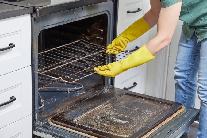 Woman wearing cleaning gloves removes oven racks for cleaning.