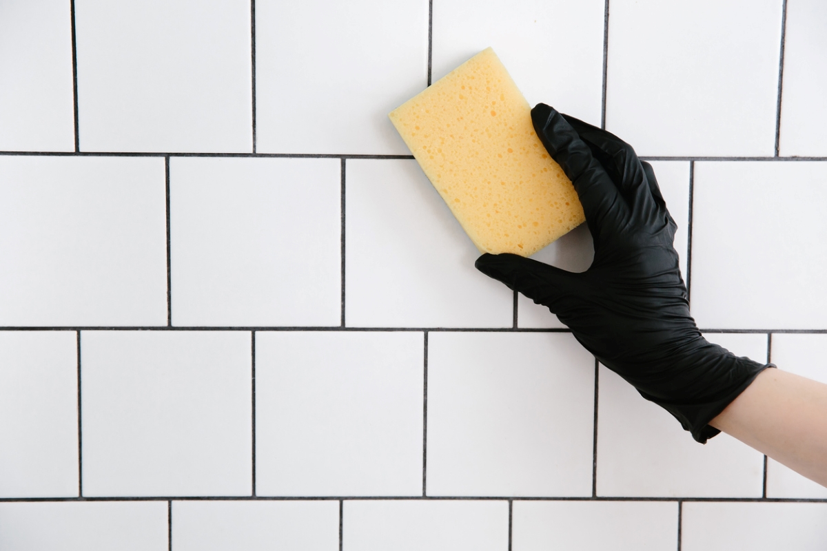 how to tile a bathroom wall - black gloved holding sponge on white tile