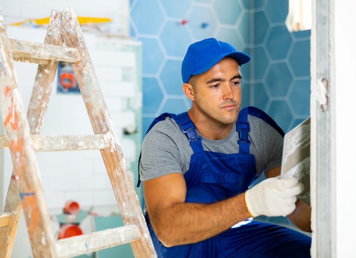 how to tile a bathroom wall - man in blue overalls looking at tile