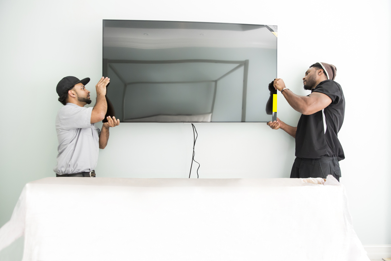 Two technicians work together mounting a TV to the wall.
