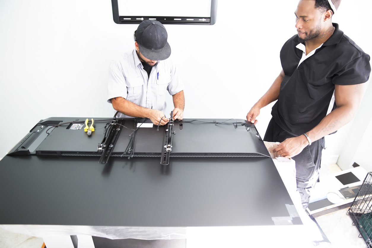Technicians work on a TV placed face down on surface before mounting.