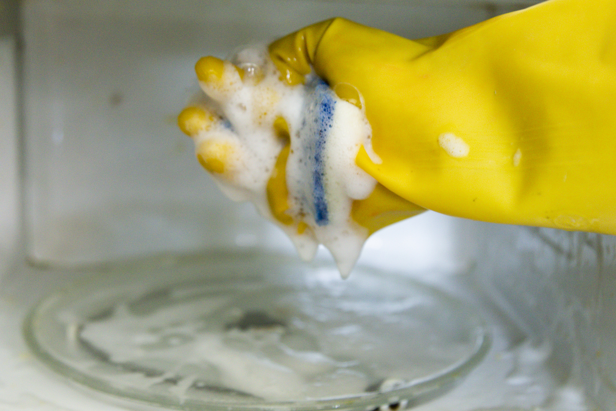 how to clean a microwave using yellow gloves and sponge to wash microwave with dish soap suds