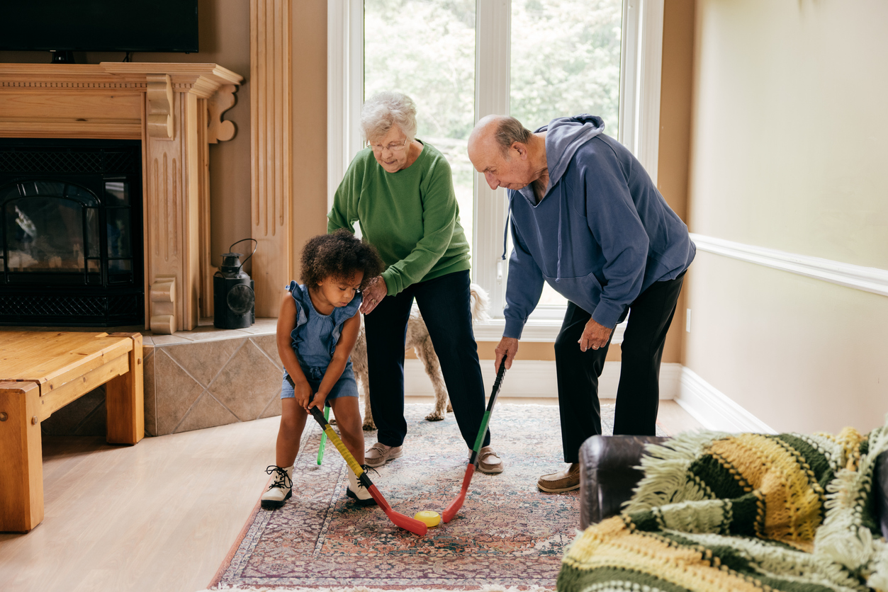 senior couple playing hockey with grandchild on persian rug in living room
