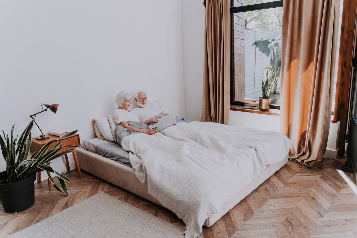 elderly couple sitting in bed with laptop in bedroom