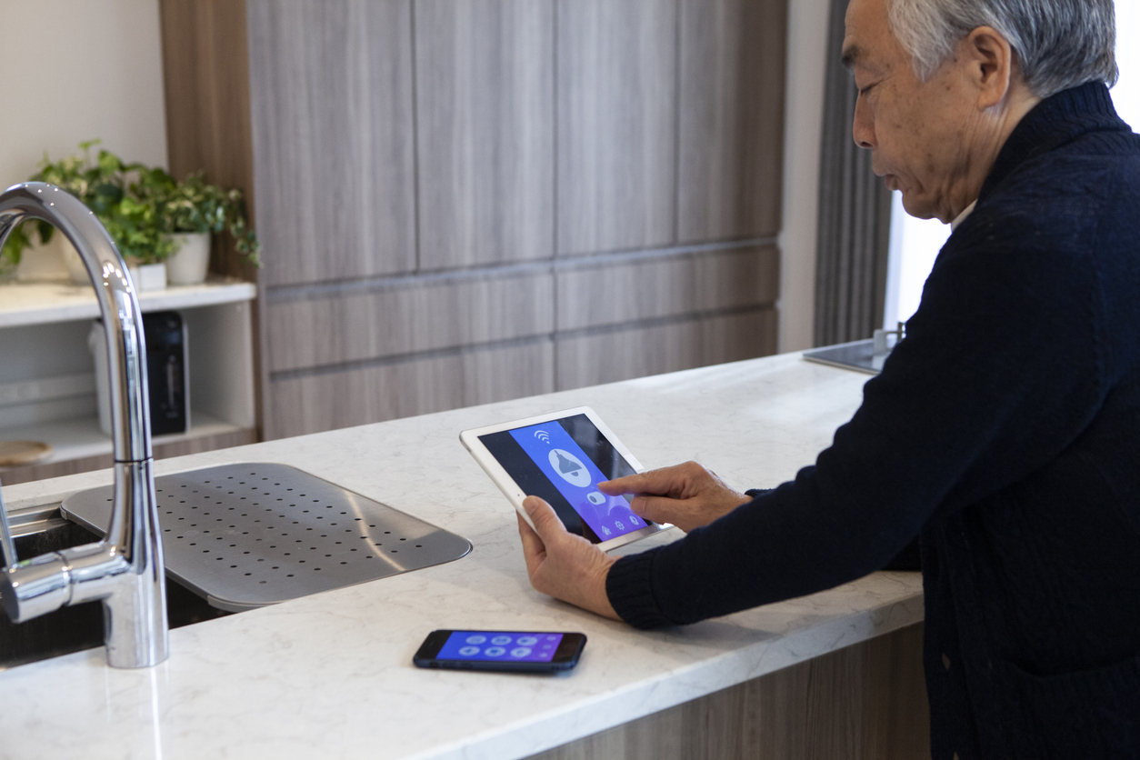 senior man uses home automation device to adjust lights in kitchen