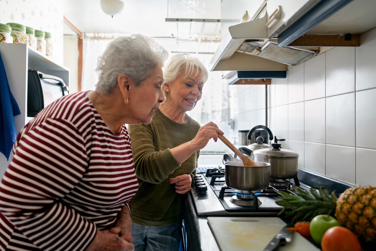 two senior women cooking together on stove in kitchen
