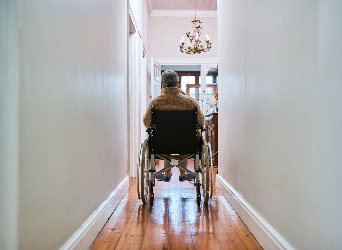 elderly man in wheel chair in hallway near staircase at home