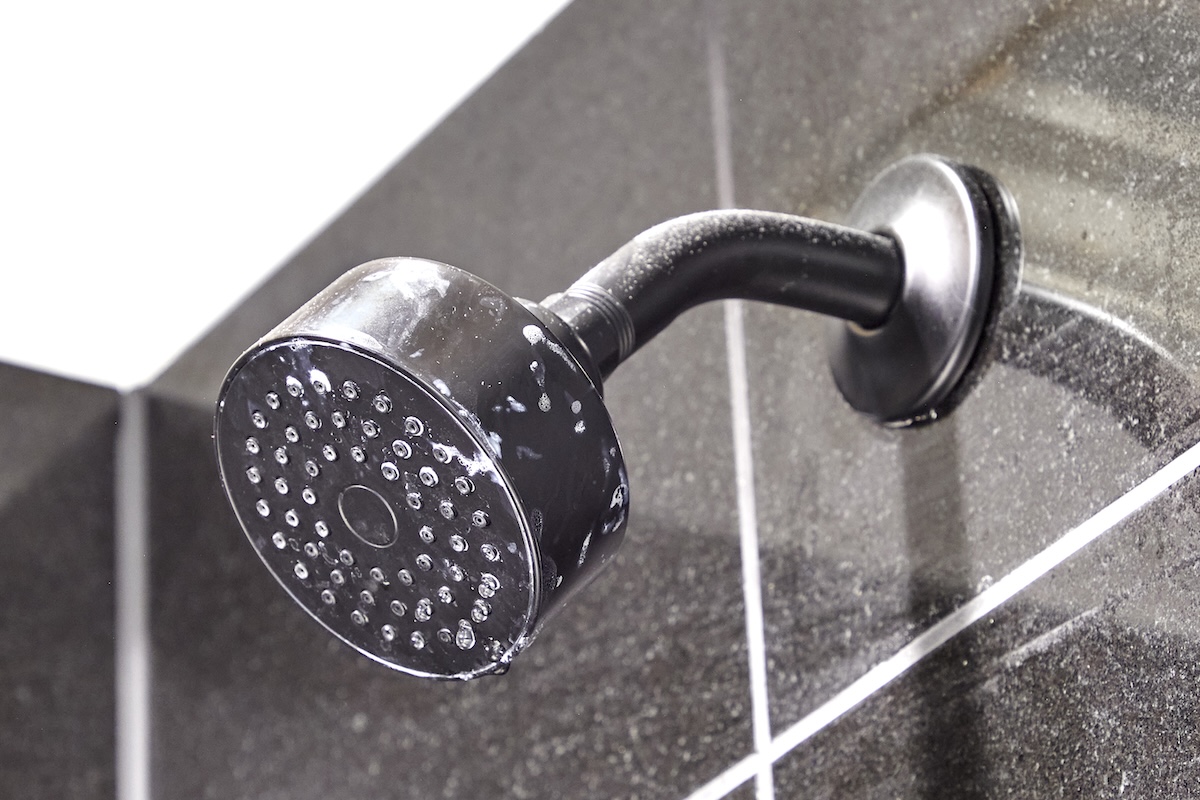 Shower head with marks attached to a grey tile wall.