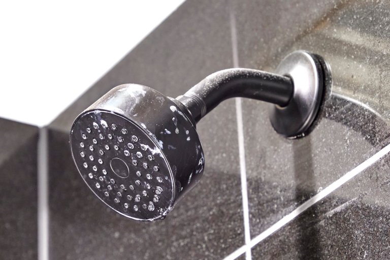 Shower head with marks attached to a grey tile wall.