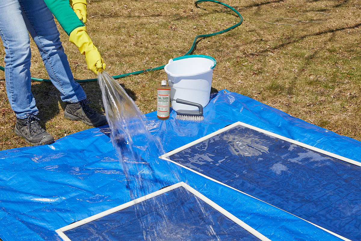 A homeowner using a hose to rinse window screens.