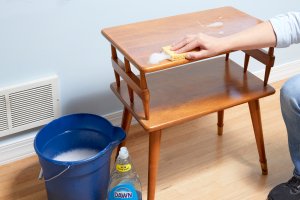 Woman cleans a small wood table with a dish soap and water solution.