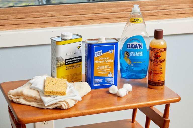 Materials needed to clean wood furniture (including mineral spirits and dish soap) collected on a small wood table.