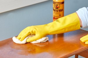 Woman wearing yellow cleaning gloves applies Feed-n-Wax to a wood table.