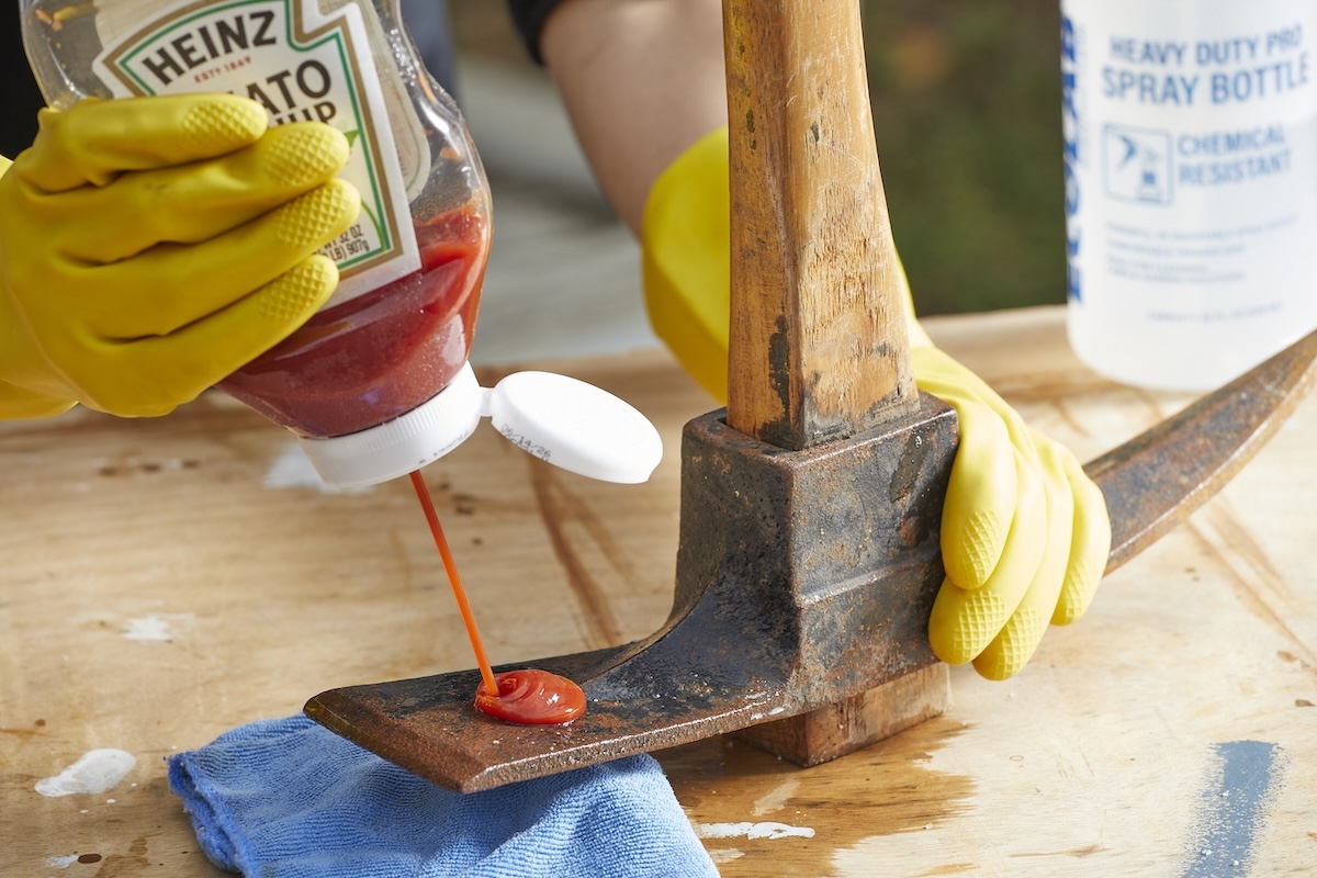 Person squirts ketchup on a rusty ax blade.