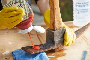 Person squirts ketchup on a rusty ax blade.