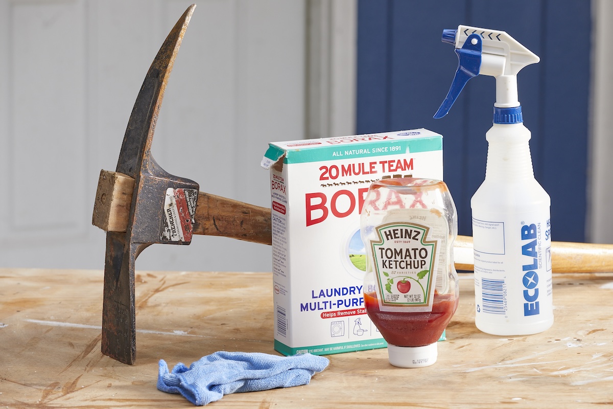 Borax, ketchup, a microfiber towel, and a rusty ax on a wood table.