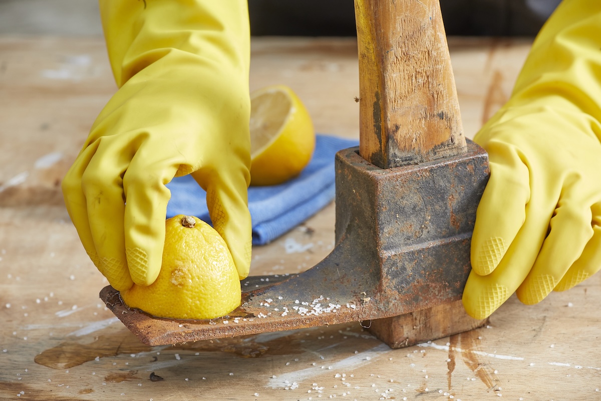 Person rubs half a lemon and salt on rusty ax blade.