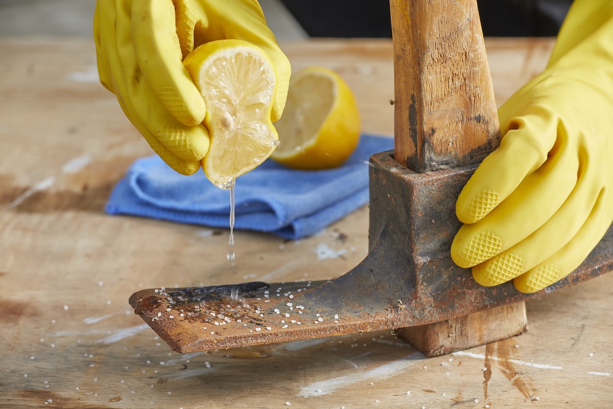 Person squeezes half a lemon on a a rusty ax blade.