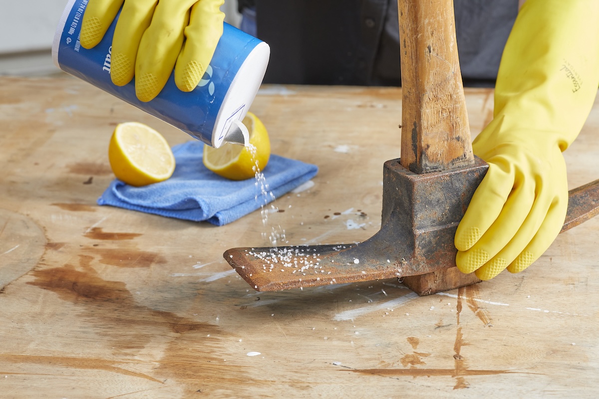 Person sprinkles salt on a rusty ax blade.