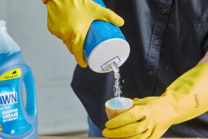 Person wearing rubber gloves sprinkles salt on a cut potato that also has dish soap on the cut.