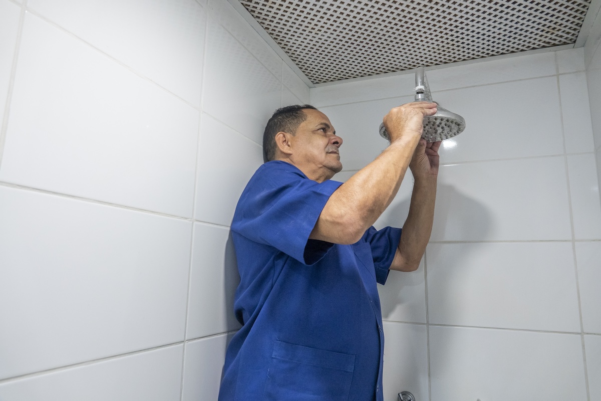 An older plumber removes a shower head.
