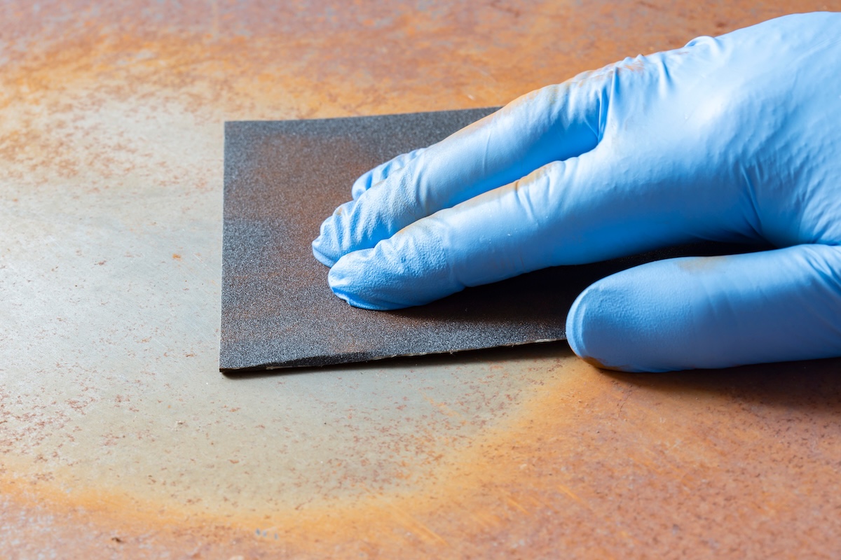 Sanding rust off sheet steel with fine grit wet and dry sandpaper.