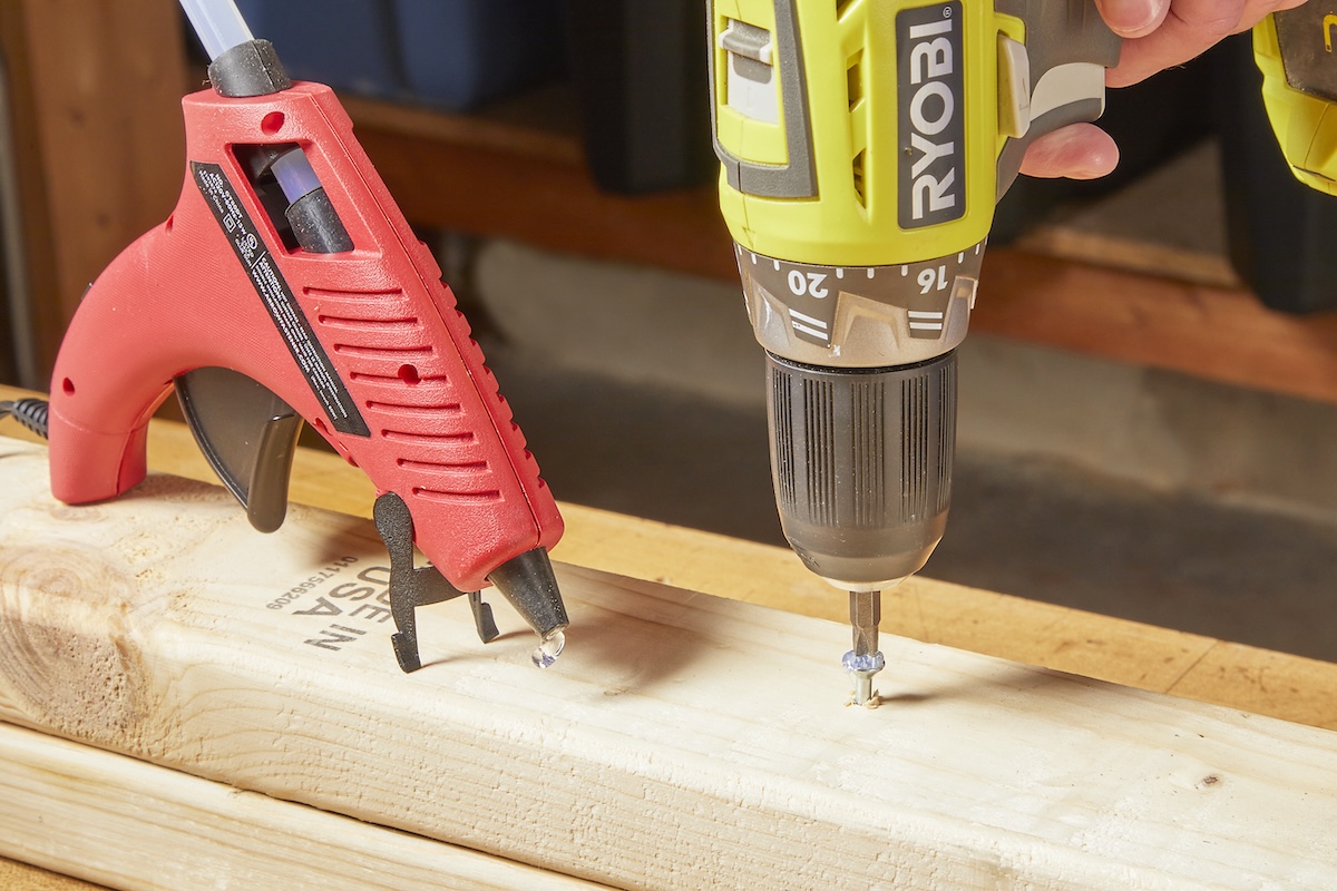 A person using a glue gun and a driver bit to remove a stripped screw stuck in a wood stud.