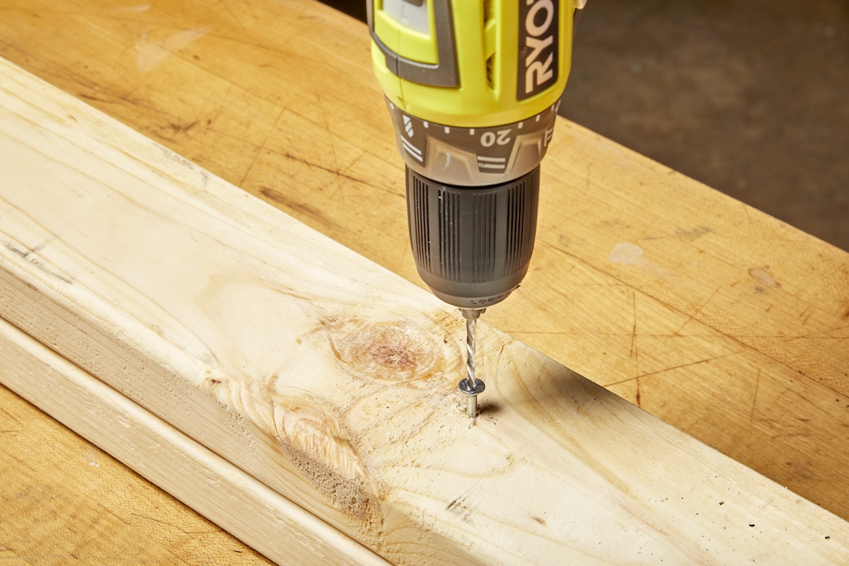 A person using a left-hand drill bit to remove a stripped screw from a wood stud in a home workshop.