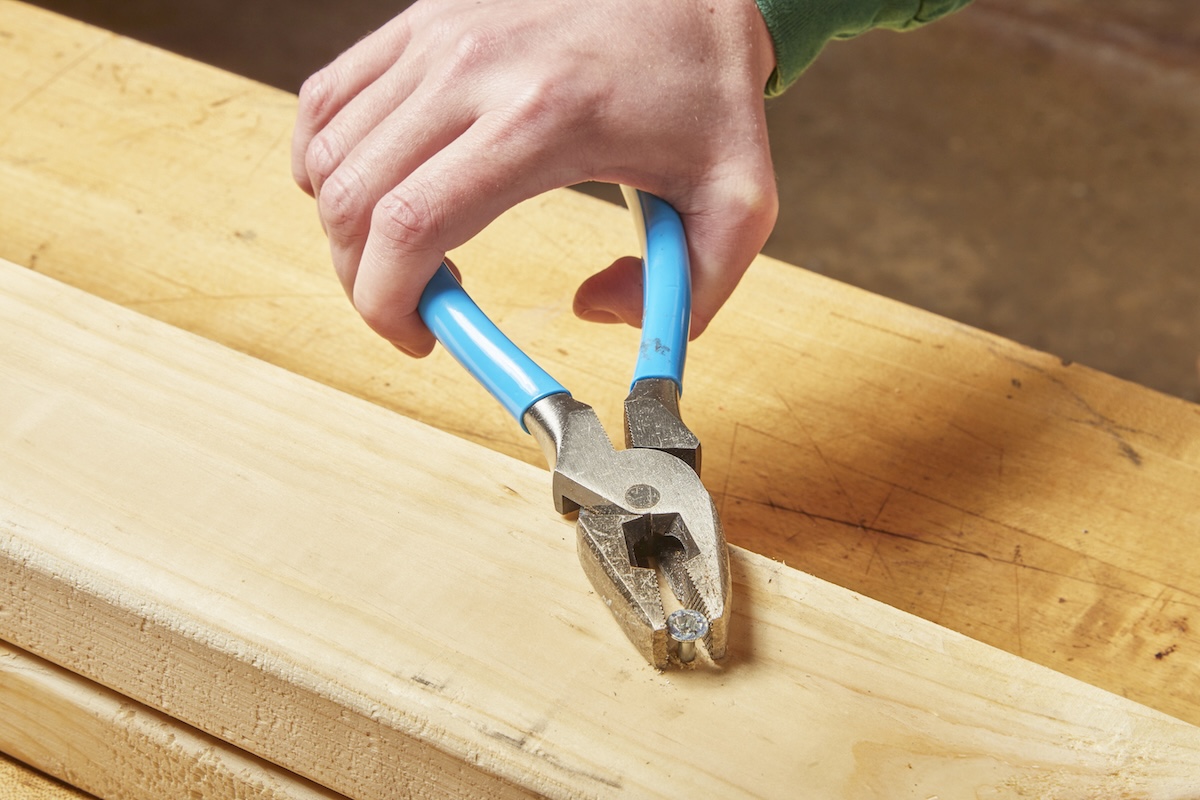 A person using a pair of pliers to remove a stripped screw stuck in a wood stud in a home workshop.