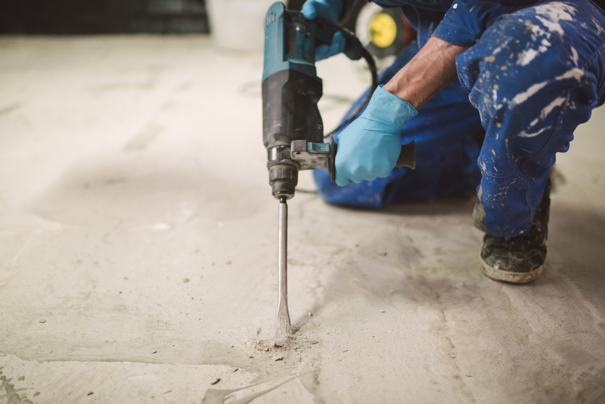 A gloved man holding a portable jackhammer is about to dig a hole in a concrete floor indoors.