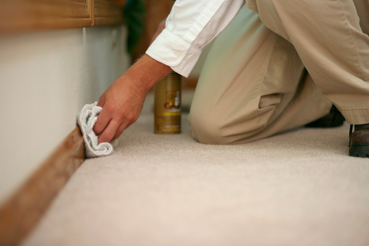 Person in white blouse and khaki pants cleaning wood baseboards