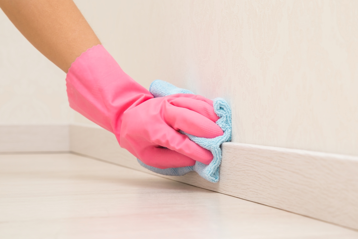Pink gloved hand wiping down baseboard
