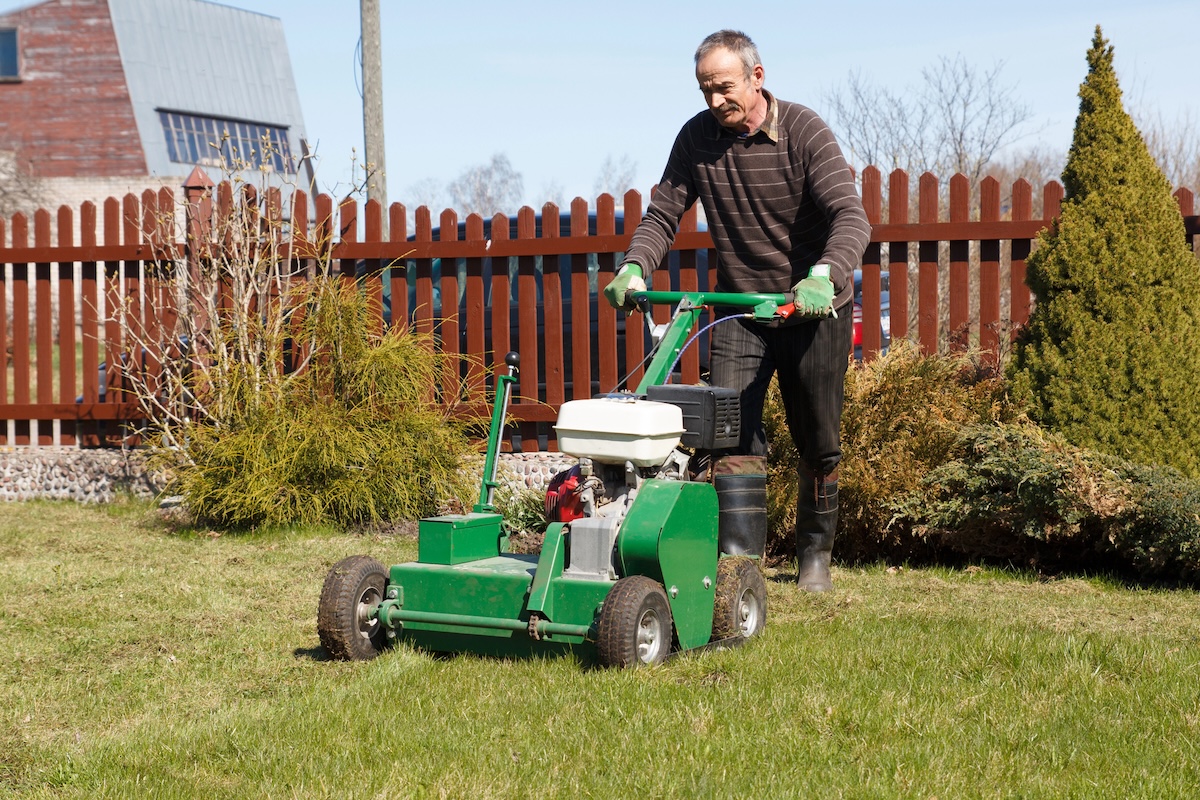 A man pushes a gas-powered core aerator across his lawn. 