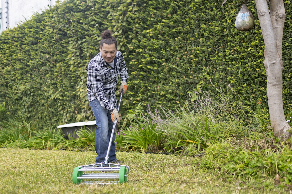 A man in a plaid shirt uses a core aerator on a green lawn .