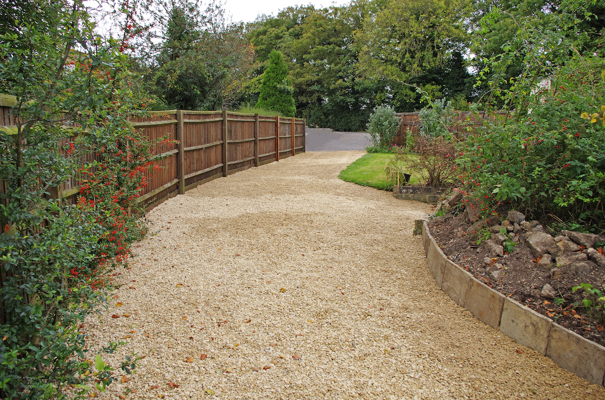 A gravel driveway with light brown stones and a brown fence on the left side. Picture taken in Swindon. Wiltshire, England