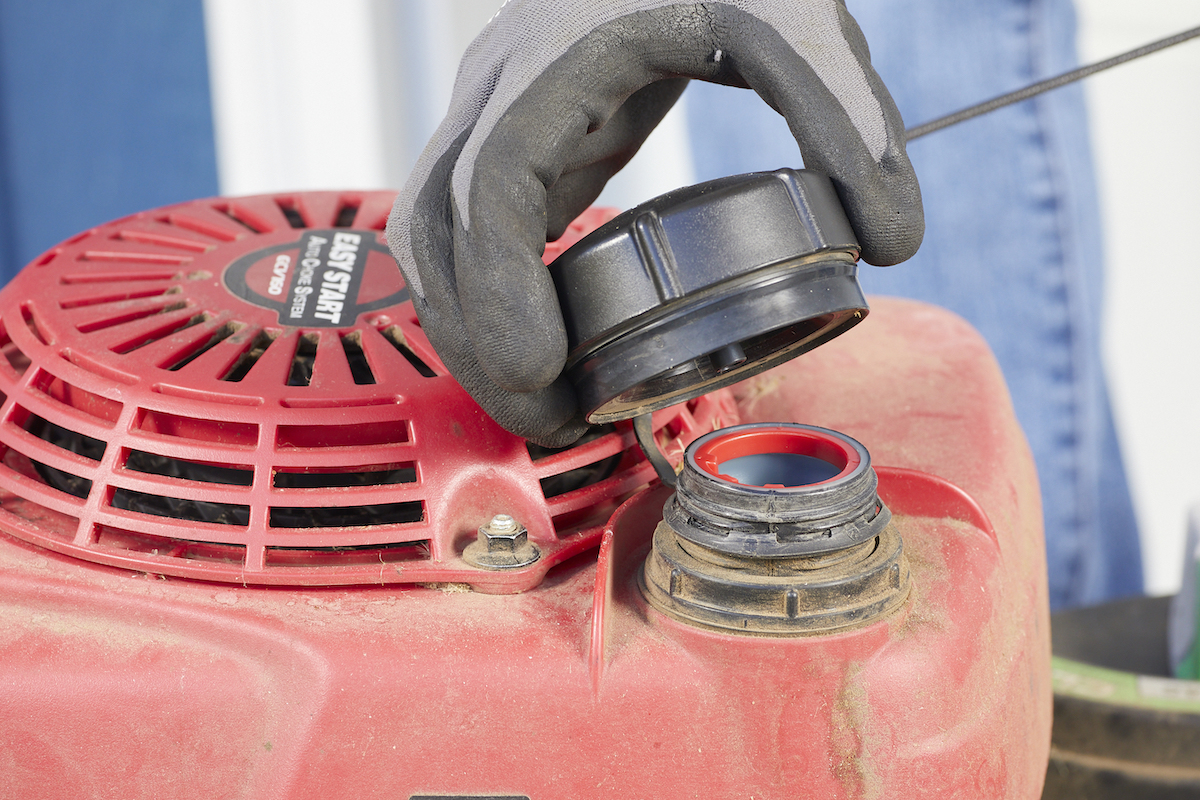 Person unscrews black gas cap on lawn mower.