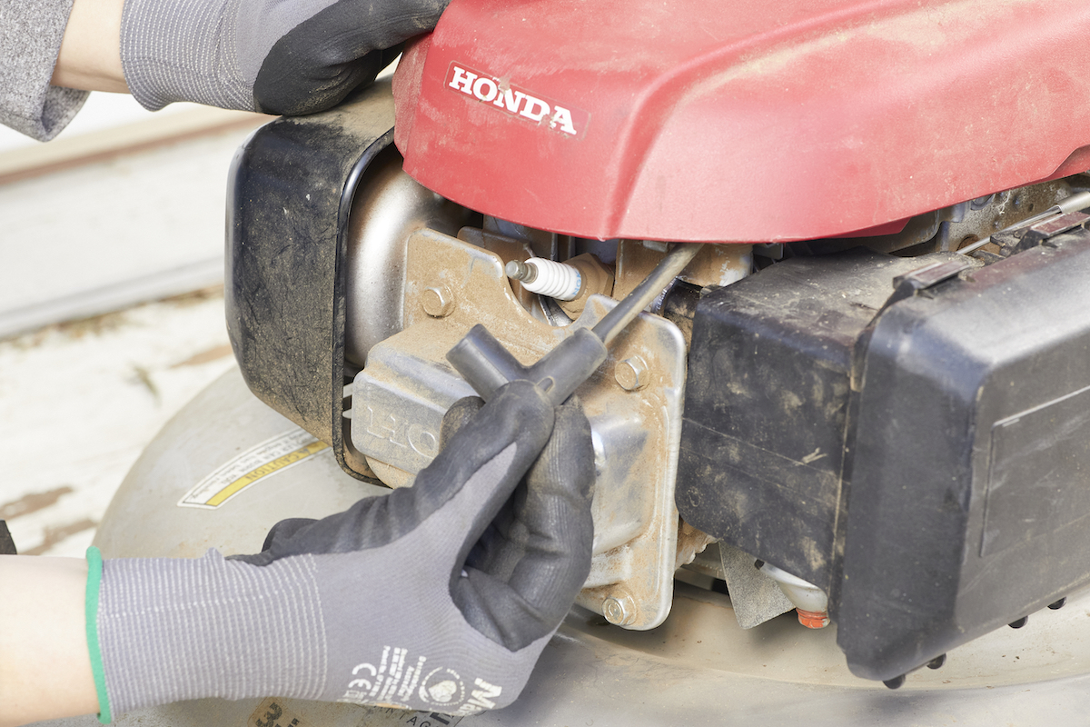 Person wearing gloves checks the spark plug on a lawn mower.