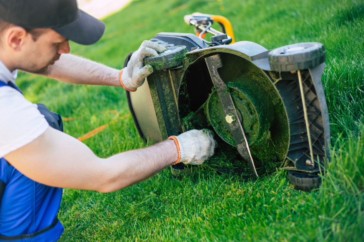 man cleaning grass clippings from lawn mower blade