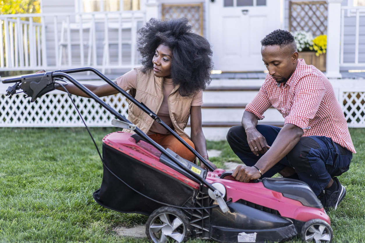 woman and man in front yard working on lawn mower