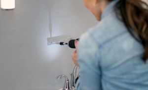 Woman drills into wall where medicine cabinet will go.