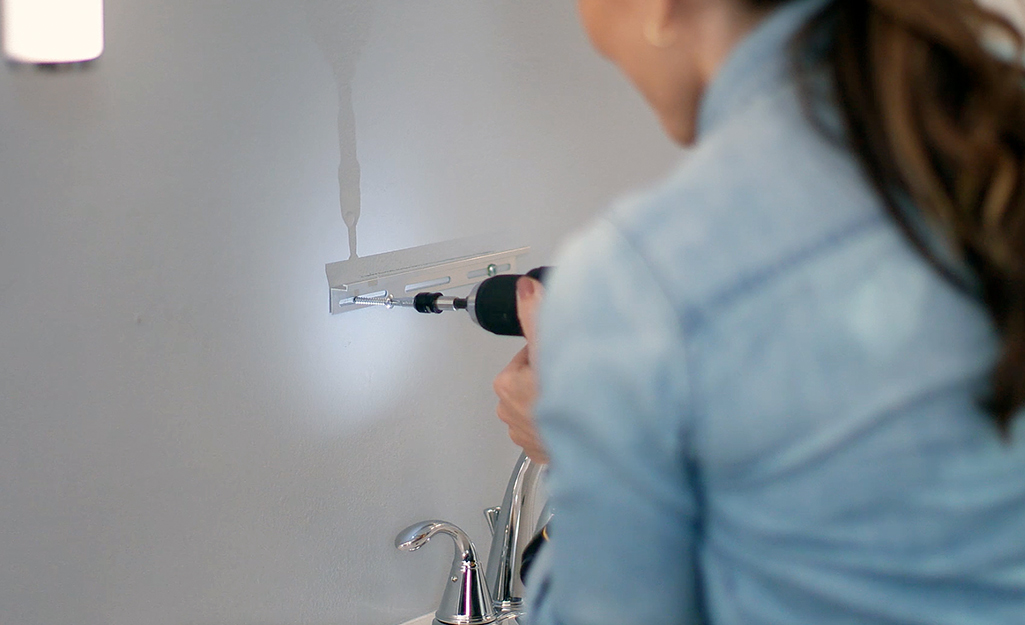 Woman drills into wall where medicine cabinet will go.