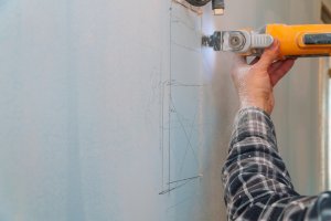 Man cuts along a line drawn on drywall using a saw.
