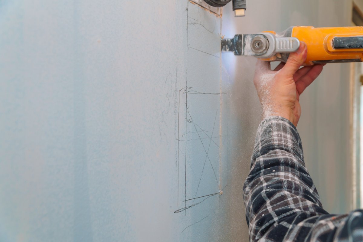 Man cuts along a line drawn on drywall using a saw.