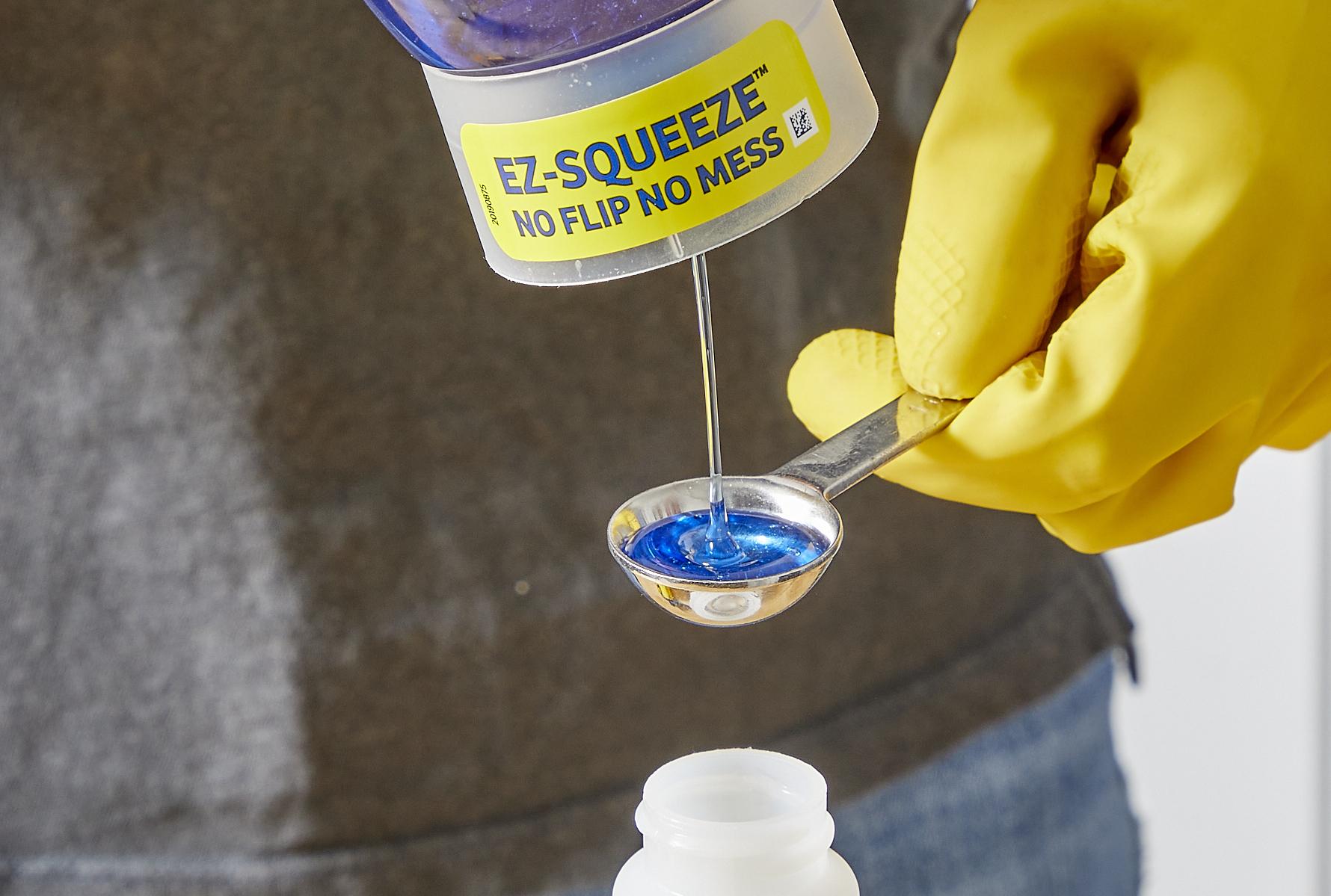 Person squeezing dish soap into a measuring spoon over a spray bottle.