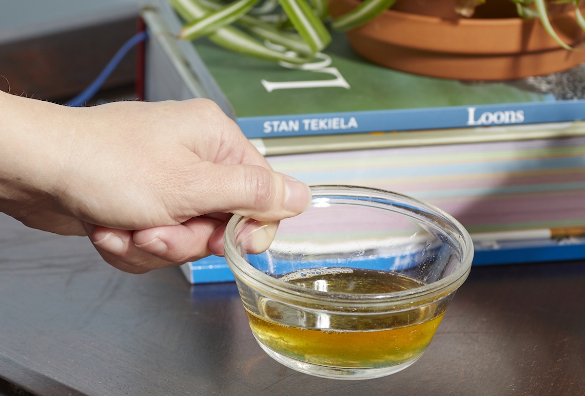Person puts small glass bowl of apple cider vinegar on a table with a book and a plant.