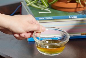 Person puts small glass bowl of apple cider vinegar on a table with a book and a plant.