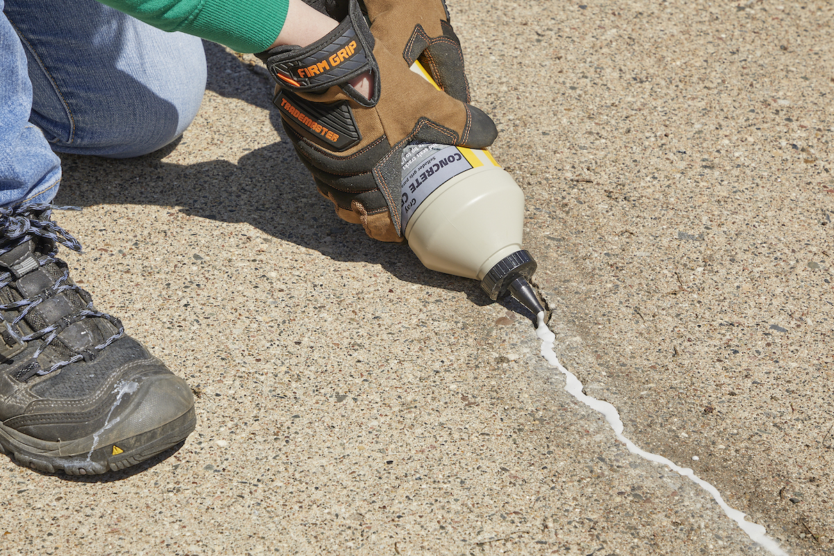 Woman squeezes concrete filler into a crack in a driveway.