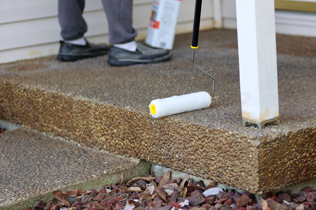Clear sealing concrete porch with a paint roller in front of a home.